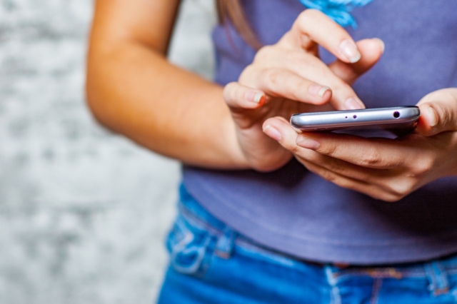young teenager girl hand using mobile phone or smartphone on gray wall background