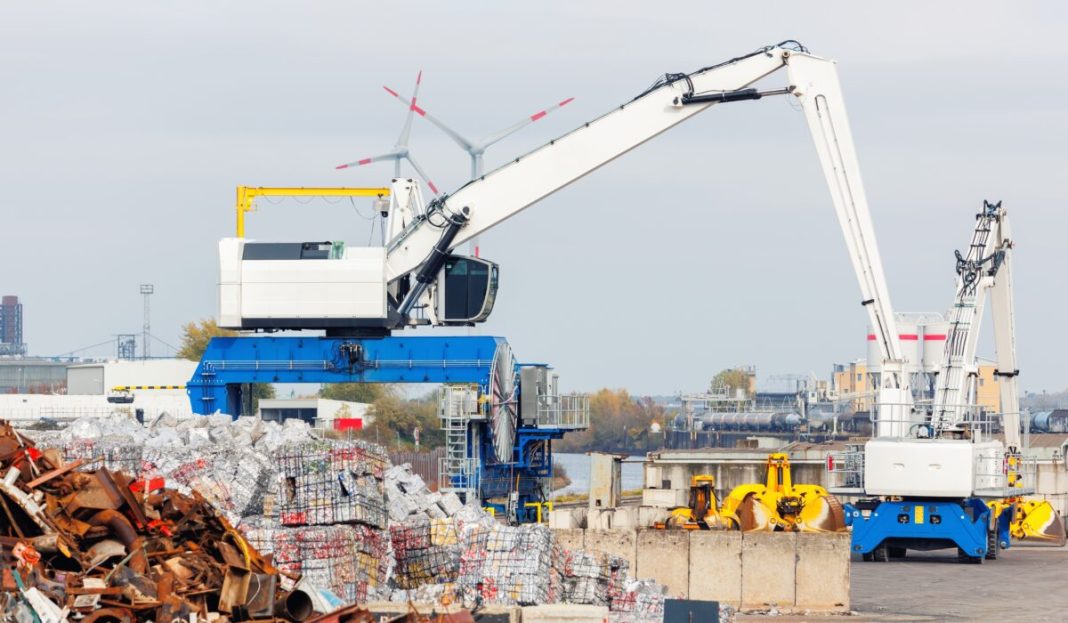 Crane,At,Recycling,Facility,Loading,Large,Scrap,Metal,Pile,With