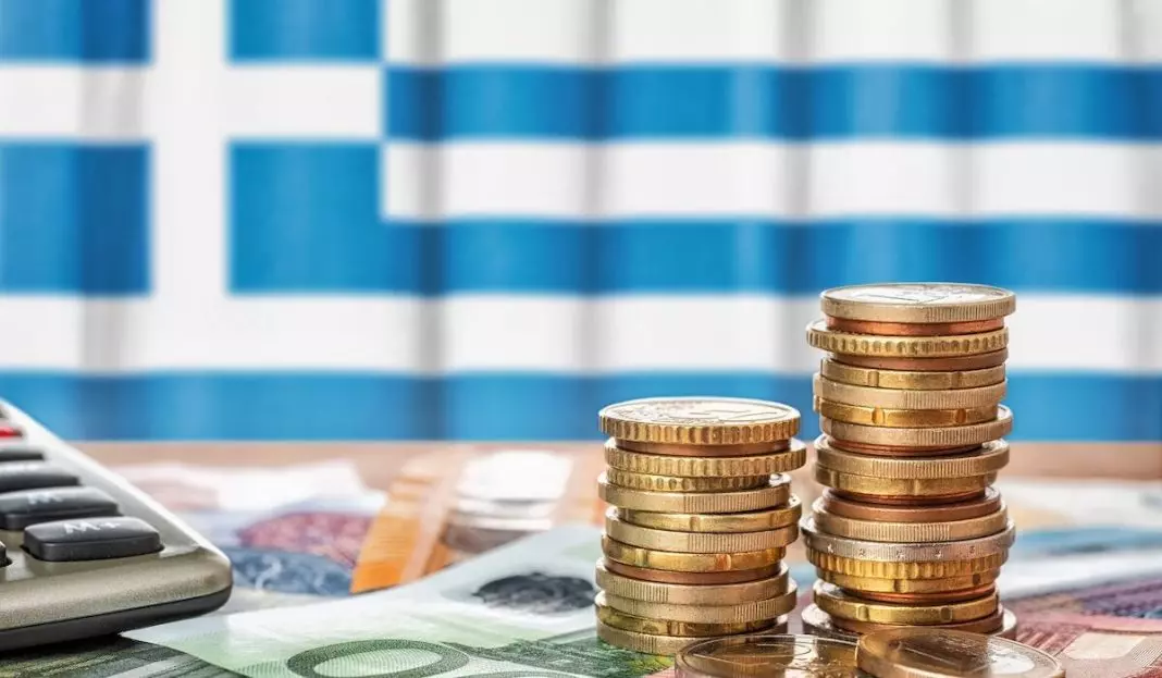 Euro banknotes and coins in front of the national flag of Greece